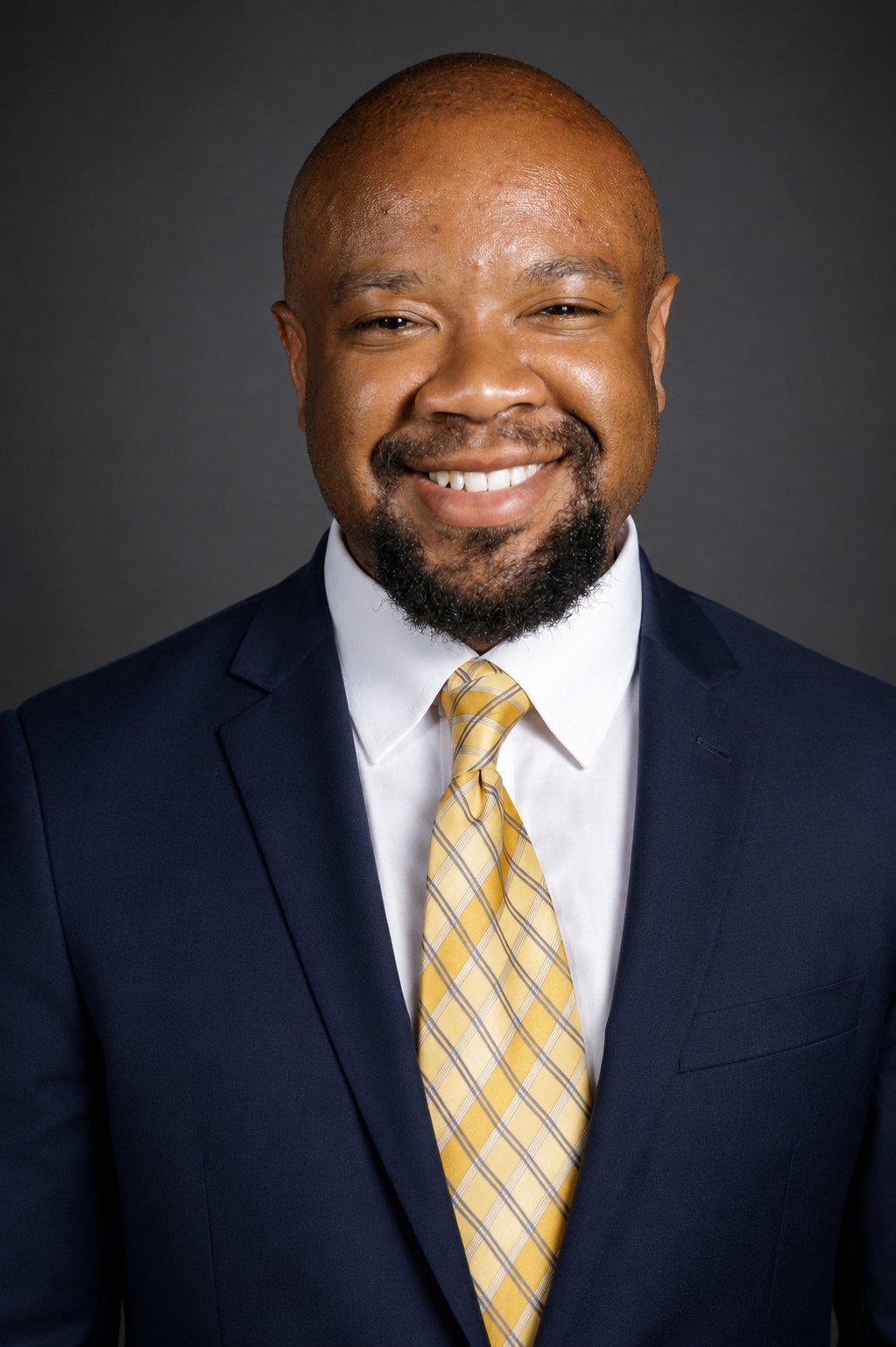 Studio headshot of Jonathon Cummings in a navy suit and gold tie